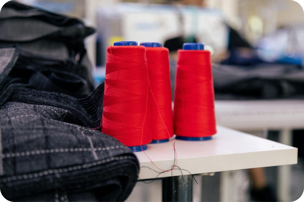 Spools of red industrial thread and folded denim in a garment production workspace that illustrates the type of environment supported by apparel manufacturing ERP software.
