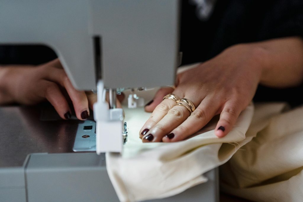 Hands guiding fabric through an industrial sewing machine during garment construction in a swimwear factory using a swimwear ERP system