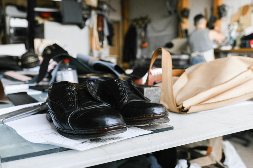 Finished leather shoes resting on a workbench next to cutting patterns and materials in a workshop, representing footwear ERP software coordinating manufacturing workflows