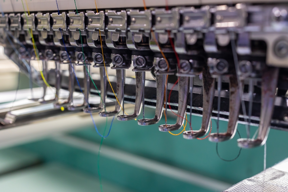 Industrial embroidery machine needles stitching fabric in a garment factory environment supported by garment manufacturing ERP software designed for production execution.