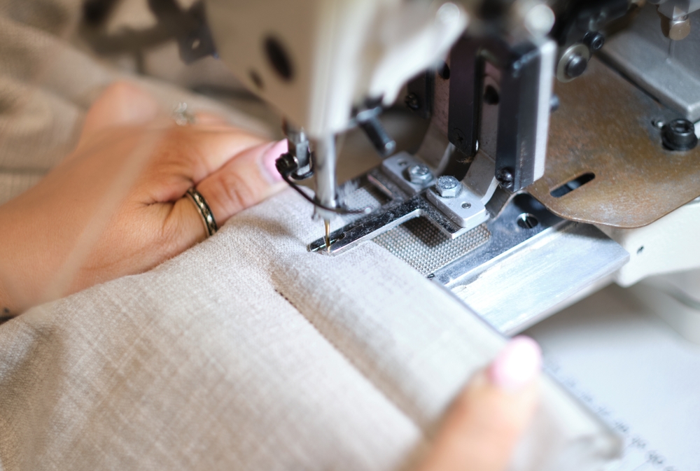 Garment worker sewing fabric on an industrial machine inside a production facility using garment manufacturing ERP software to manage real-time WIP and variation control.