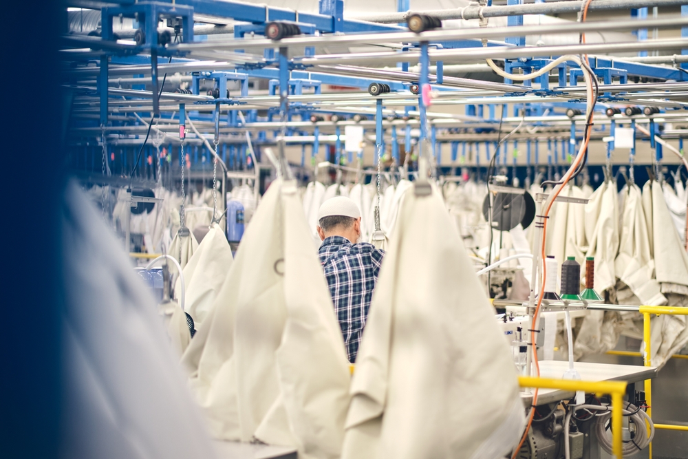 Fashion manufacturing facility with garments on overhead conveyor system, supported by an ERP for the fashion industry to manage production workflows and inventory