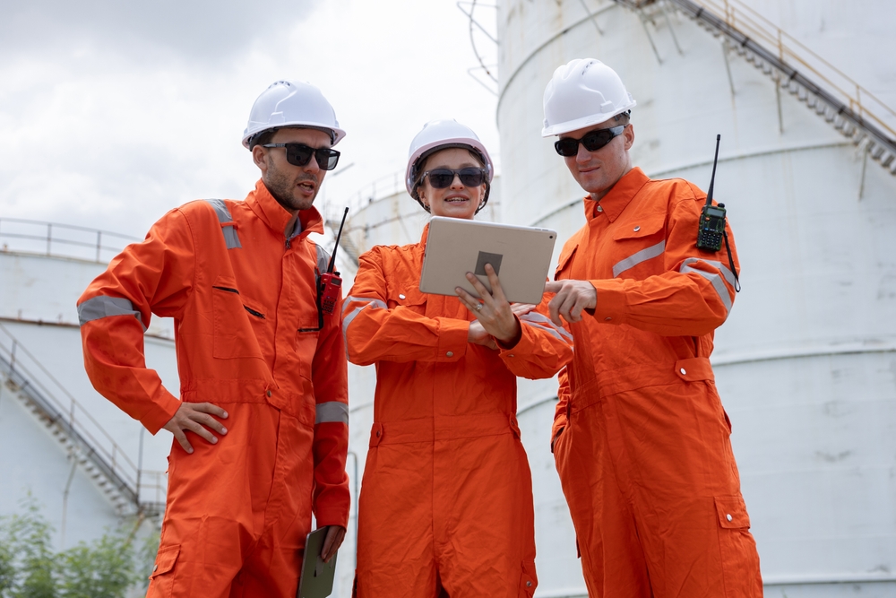 Industrial workers wearing orange safety coveralls manufactured using PolyPM, a uniform manufacturing software developed by Polygon Software for workwear and uniform production.