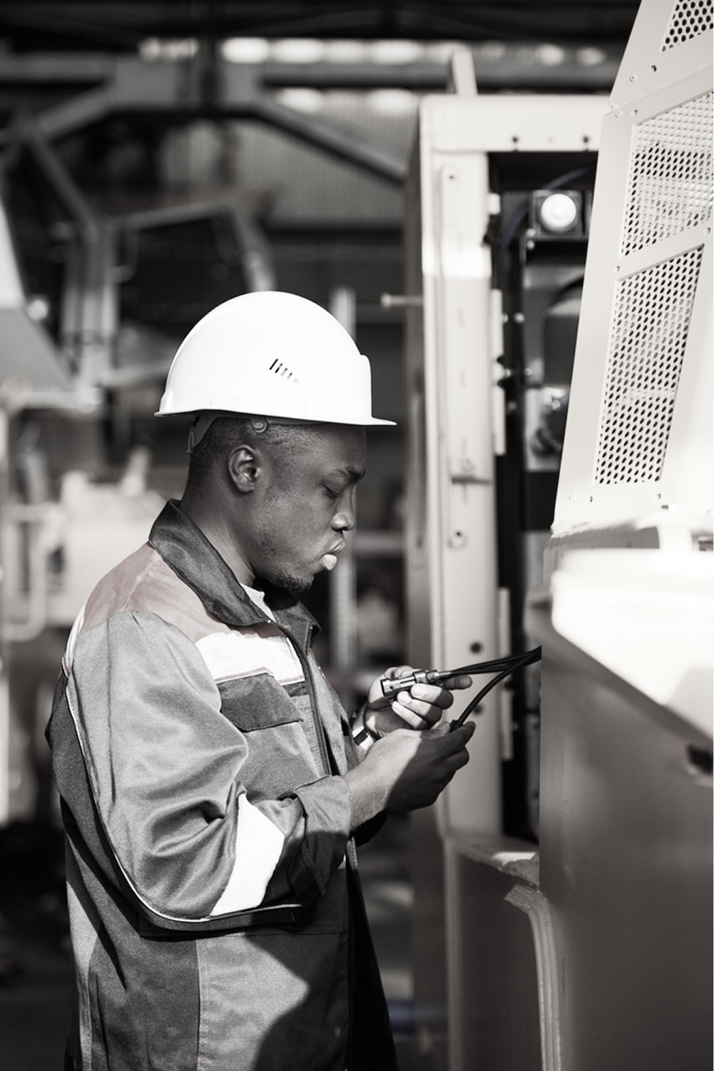 Worker in branded workwear and white hard hat inspecting industrial equipment in a manufacturing facility, with workwear programs managed by PolyPM by Polygon Software, a workwear ERP.