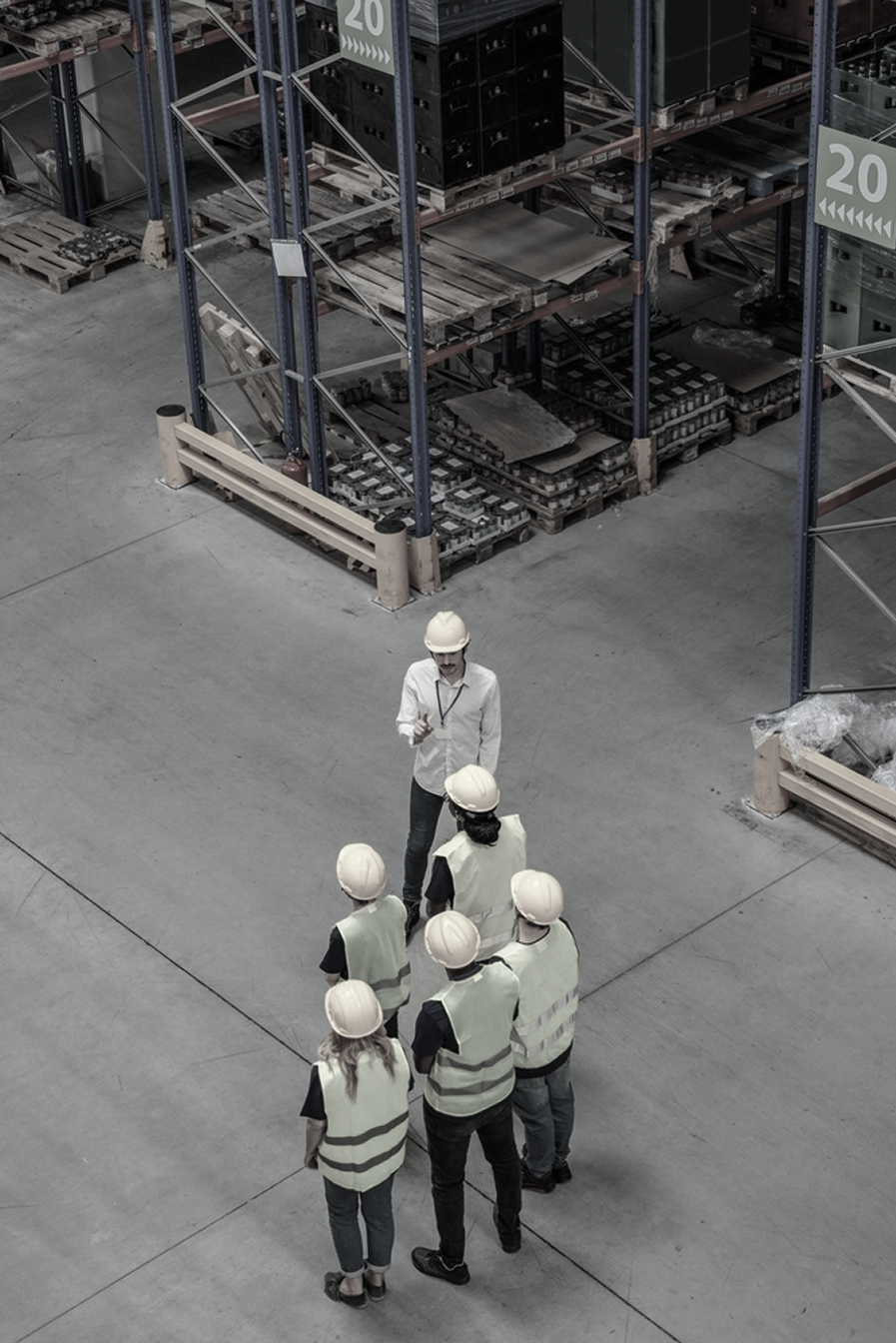 Workers in hi-visibility safetywear and hard hats inside a warehouse, with compliance managed by PolyPM by Polygon Software, a safetywear ERP.
