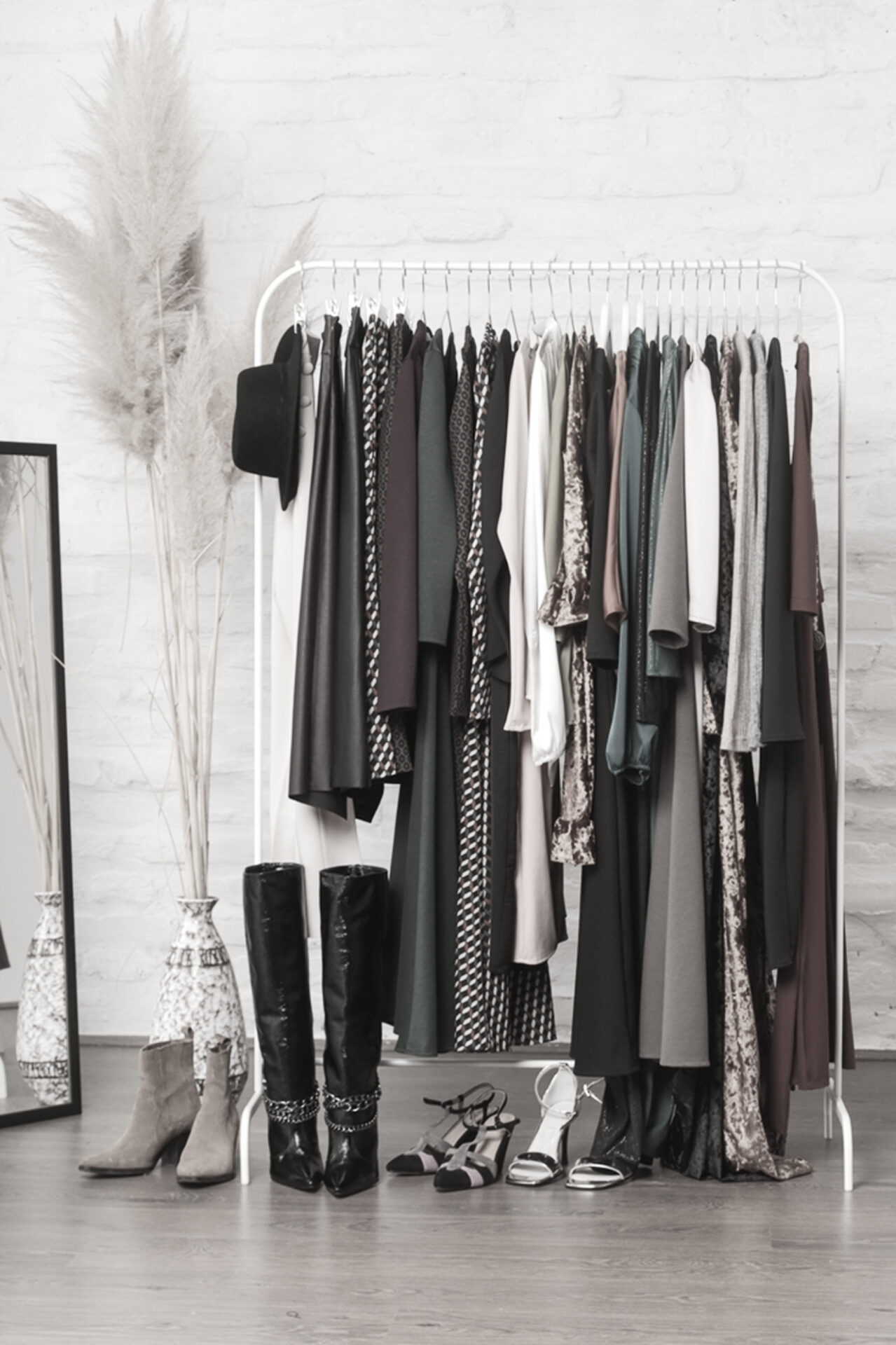Curated fashion collection on a clothing rack with dresses, jackets, boots, and heels styled in a showroom, with collection production managed by PolyPM by Polygon Software, fashion ERP software.