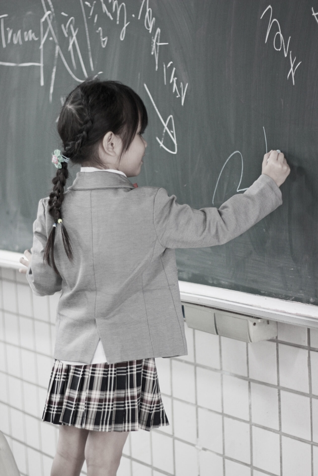 School uniform featuring a grey blazer and plaid pleated skirt worn in a classroom, with school uniform production managed by PolyPM by Polygon Software, an ERP uniforms manufacturers rely on.