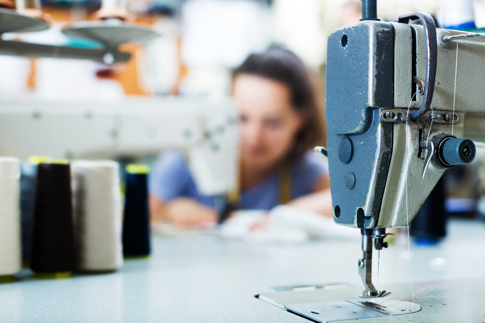 Automated sewing and cutting machinery running in a modern factory environment integrated with product lifecycle management software fashion.