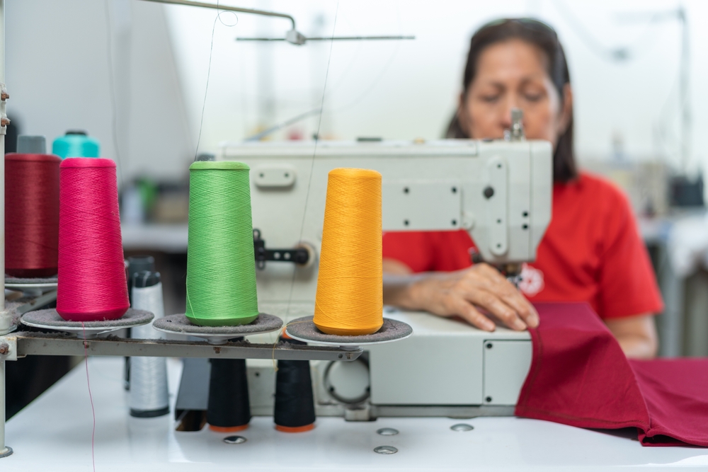 Operator guiding fabric through an apparel manufacturing machine monitored by manufacturing ERP software