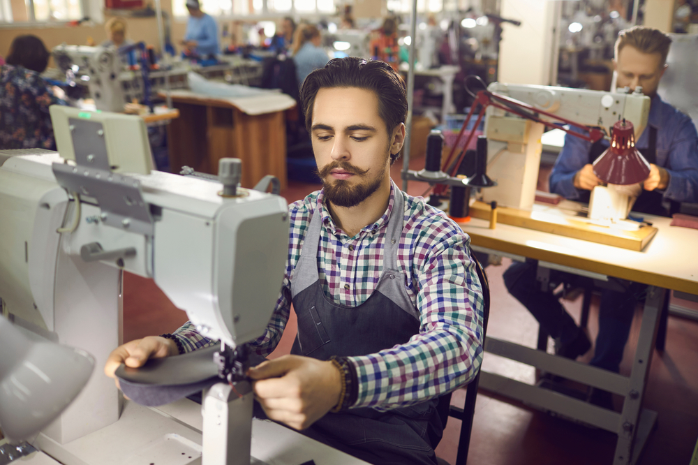 Operator at an industrial sewing machine in a garment factory using manufacturing inventory management software.
