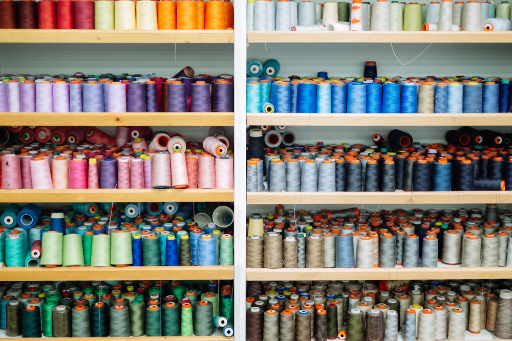 Rolls of thread stacked in a warehouse tracked by manufacturing inventory management software.