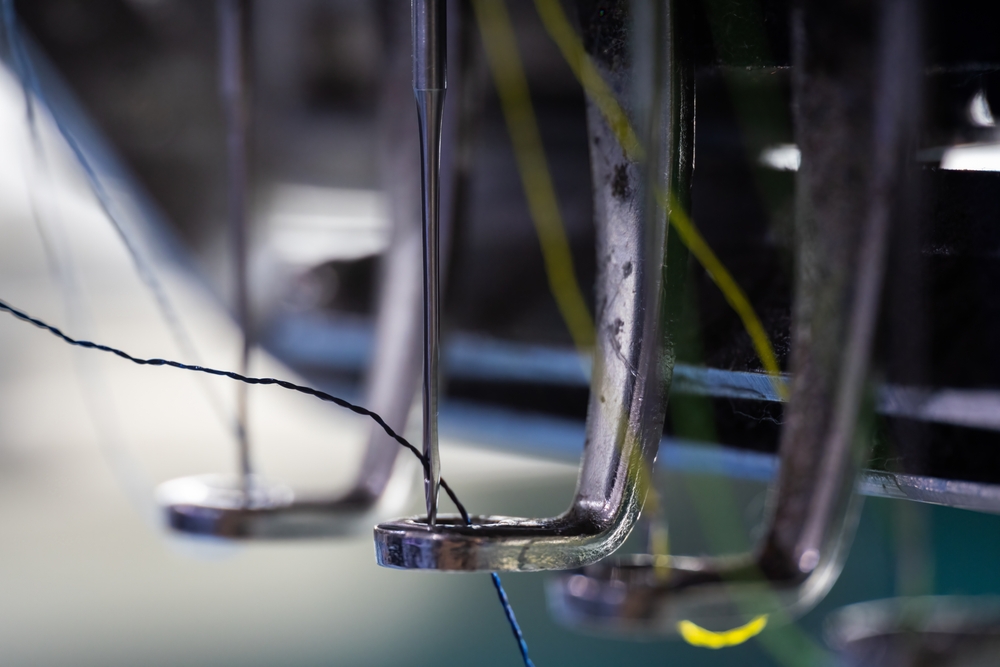 Close up of an industrial clothing manufacturing machine stitching to the seam allowance in a tech pack

